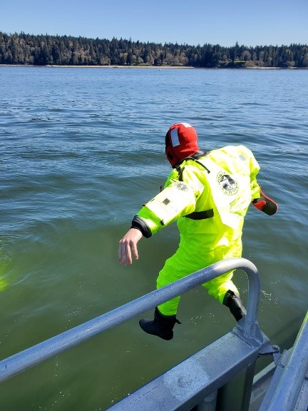 Police officer in high visibility gear jumps off a boat into water.