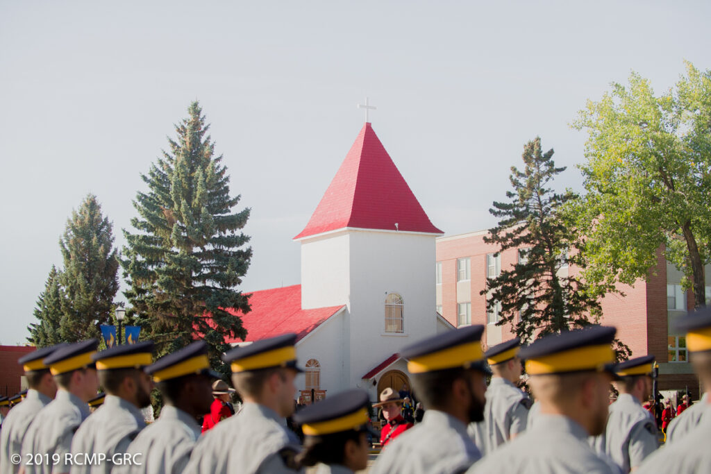 Image of RCMP Members in training outside on Depot grounds, lined up in front of a church.