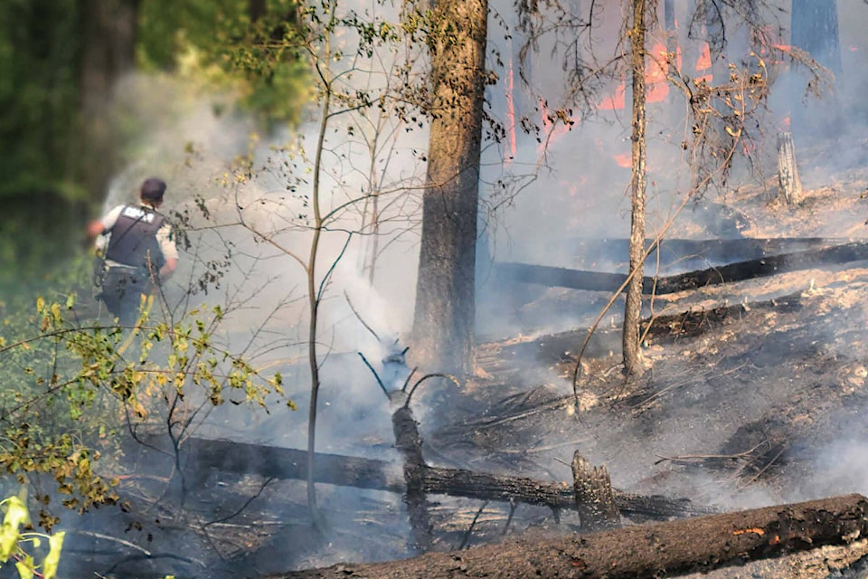 Cst. Mark Tataryn runs a water hose toward an active forest fire. (Photo: Golden RCMP)  