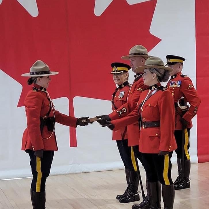 Gracie's parents present her with her badge at Depot Graduation in front of large Canadian flag